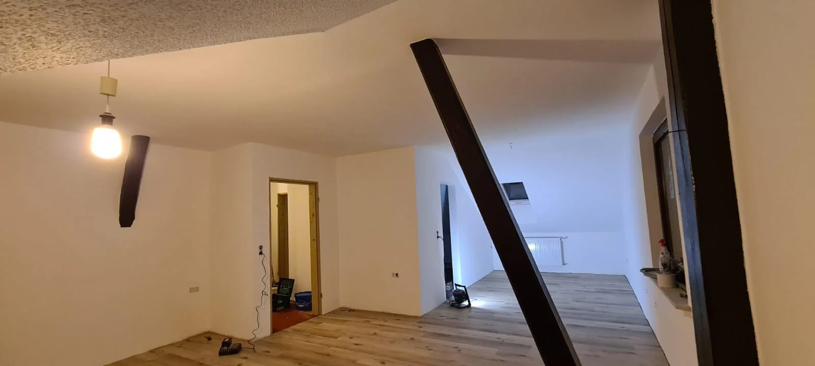Dachgeschoss mit hellen Wänden, sichtbaren Holzbalken und neuem Boden in Holzoptik